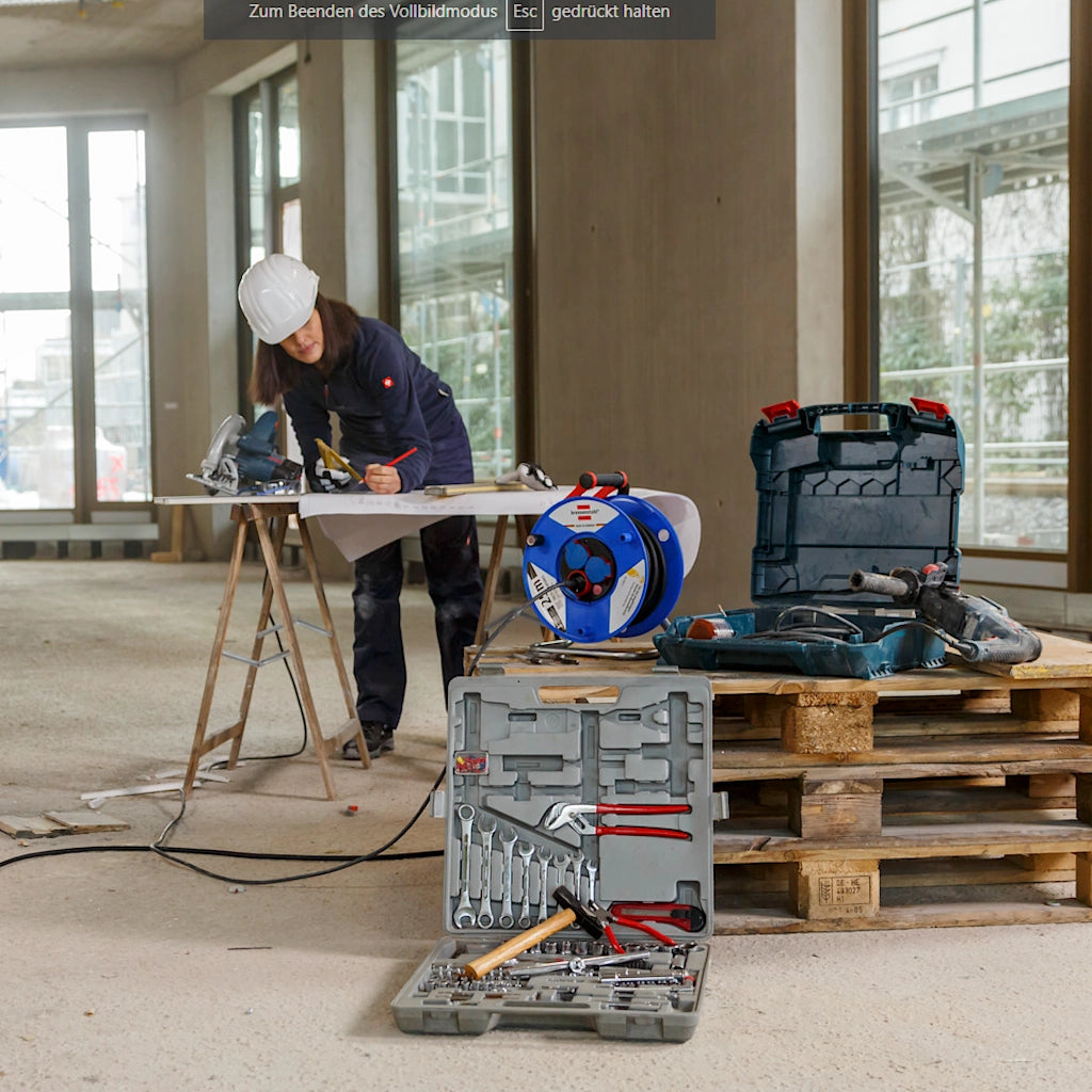 Eine Frau zeichnet auf einer Baustelle einen Plan und vor ihr befinden sich Werkzeuge und eine Kabeltrommel von Brennenstuhl