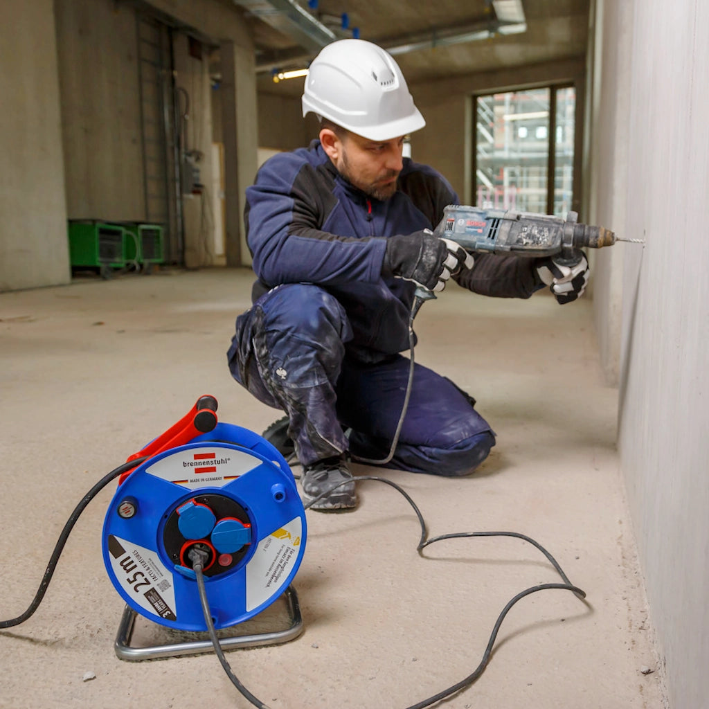 Ein Mann kniet mit einer Bohrmaschine in der Hand vor einer Betonwand und setzt zum Bohren an