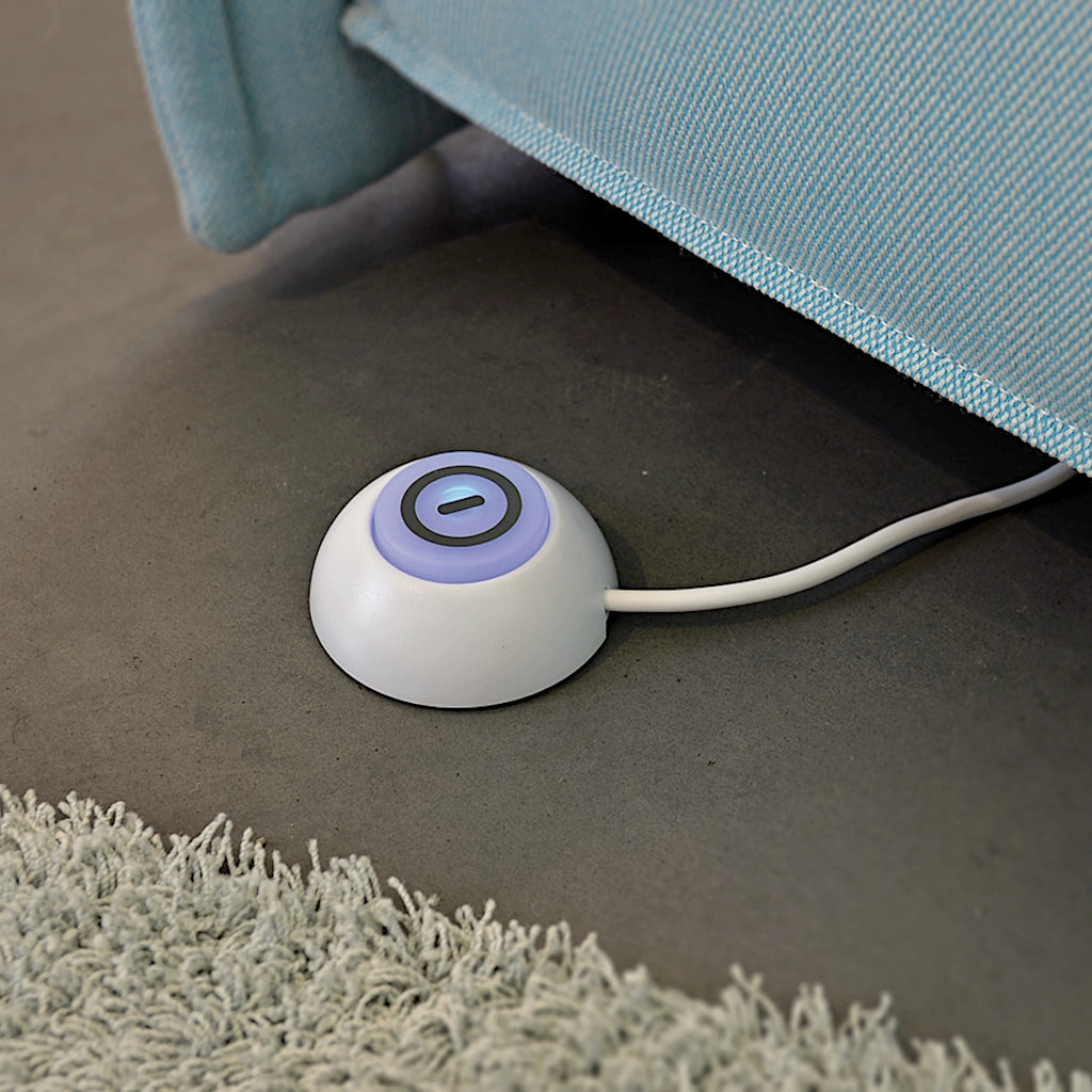 Der Fußschalter des Steckdosenadapters liegt auf dem Boden einer Wohnung neben einem Sofa.