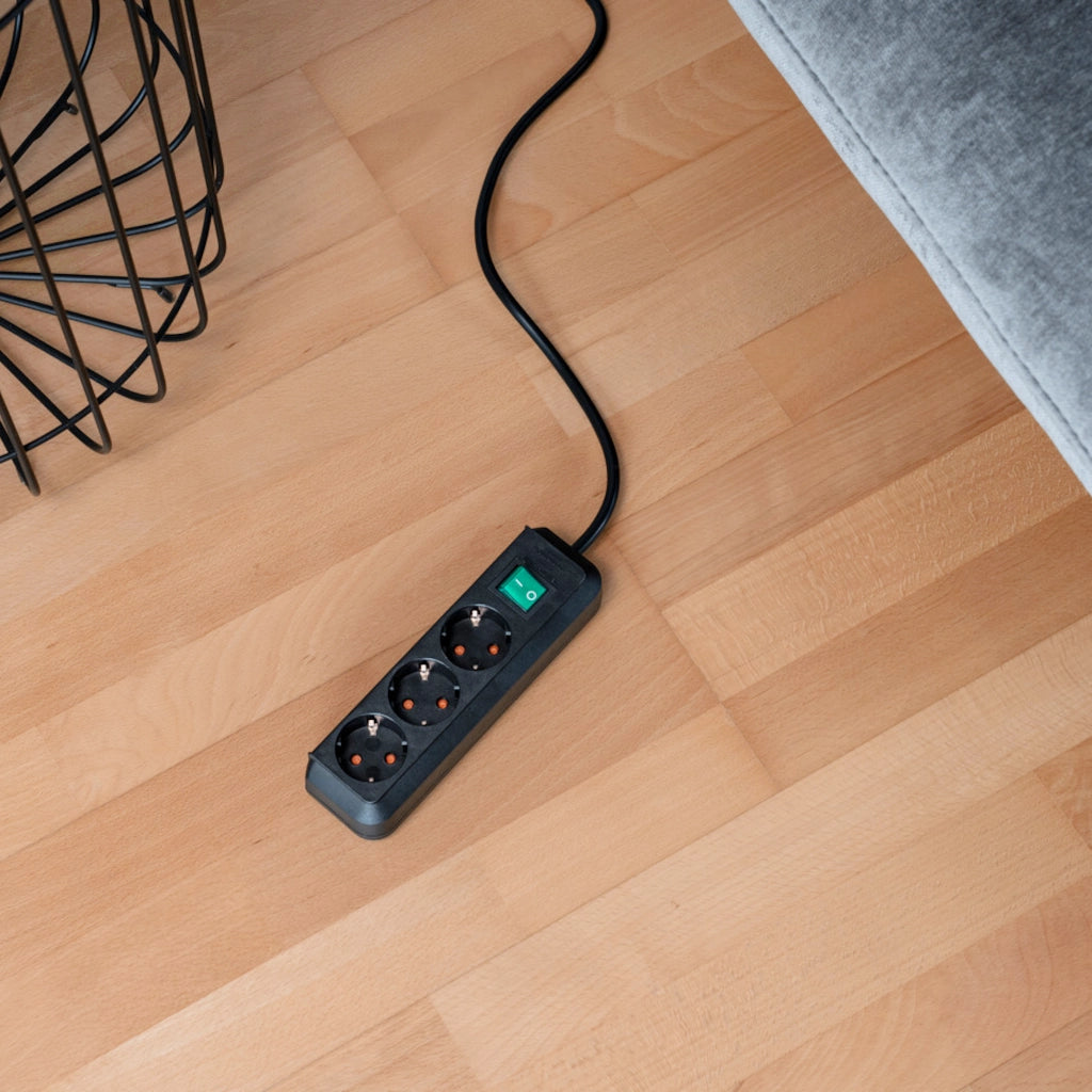 Eine schwarze Brennenstuhl Eco-Line Steckdosenleiste 3-fach mit Schalter liegt auf einem Holzfußboden