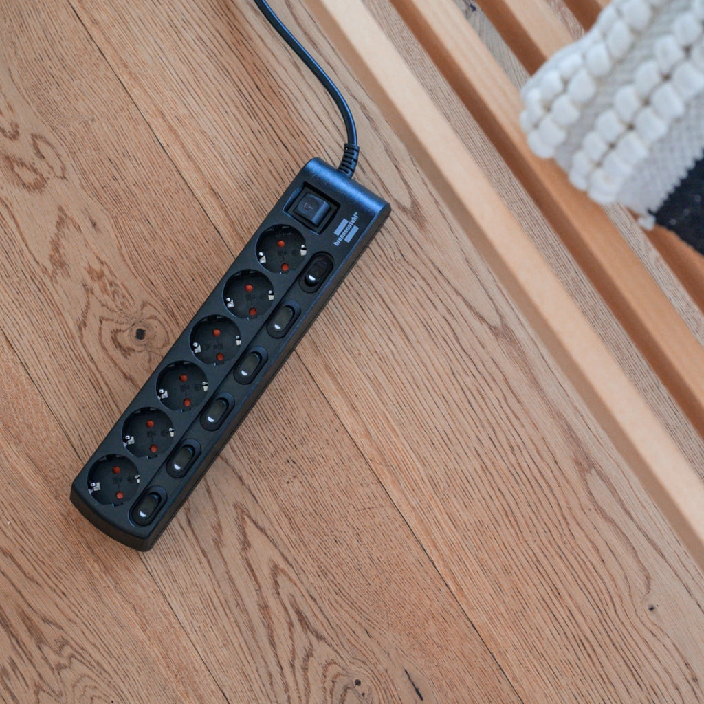 Eine schwarze Brennenstuhl 6-fach Steckdosenleiste liegt auf einem Holzfußboden