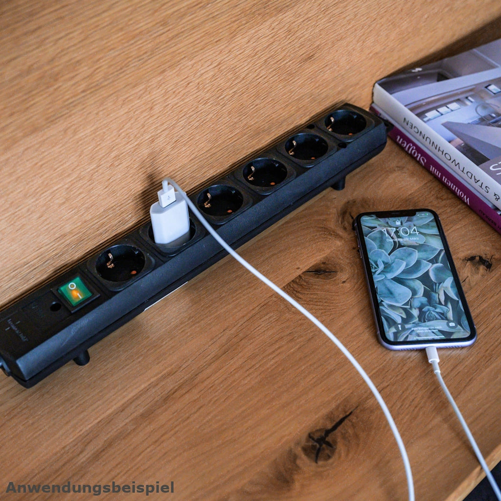 Eine Brennenstuhl Steckdosenleiste 6-fach mit Schalter liegt auf einem Holztisch und ein Ladegerät vom Handy ist eingesteckt
