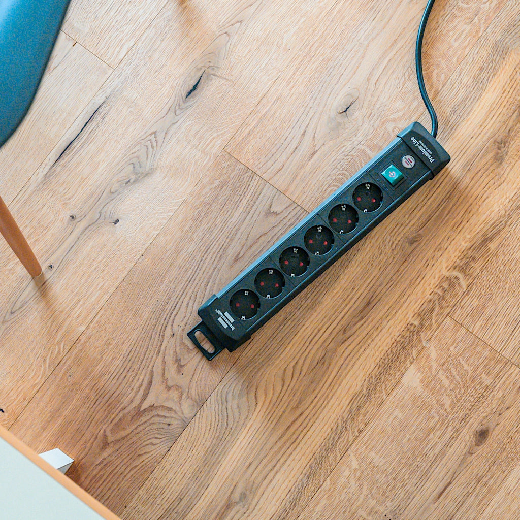 Eine schwarze Brennenstuhl Steckdosenleiste 6-fach mit Schalter liegt auf einem Holzfußboden