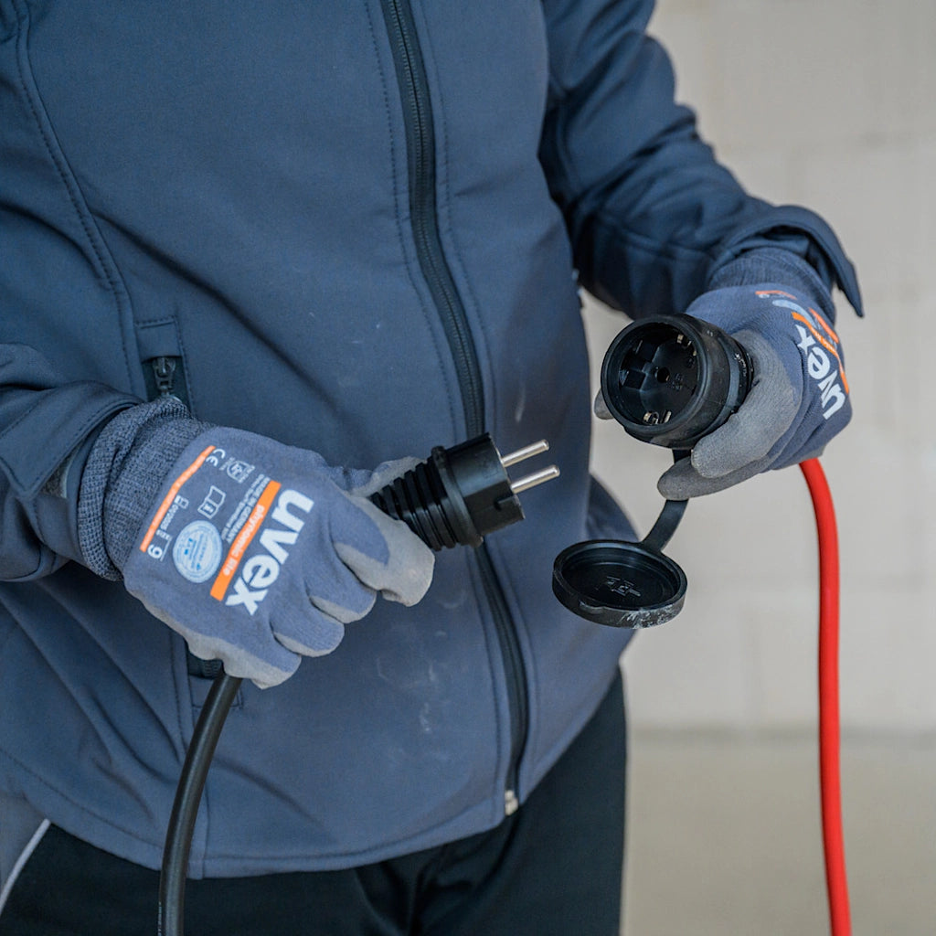 Ein Mann in blauer Arbeitskleidung hat einen Stecker und eine Kupplung von einem Verlängerungskabel in der Hand
