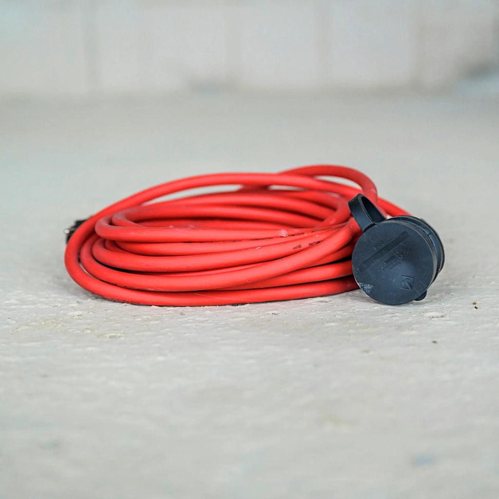Ein rotes Verlängerungskabel liegt zusammengerollt auf dem Betonboden einer Baustelle.