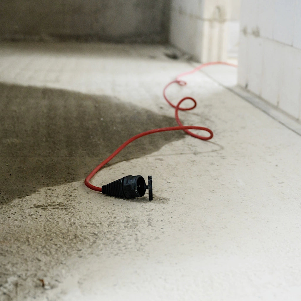 Ein rotes Verlängerungskabel liegt ausgerollt auf dem Betonboden eines Rohbaus.