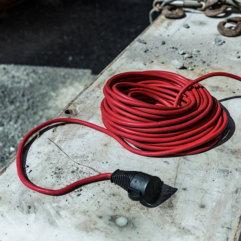 Ein rotes Verlängerungskabel liegt zusammengerollt auf dem Betonboden einer Baustelle.