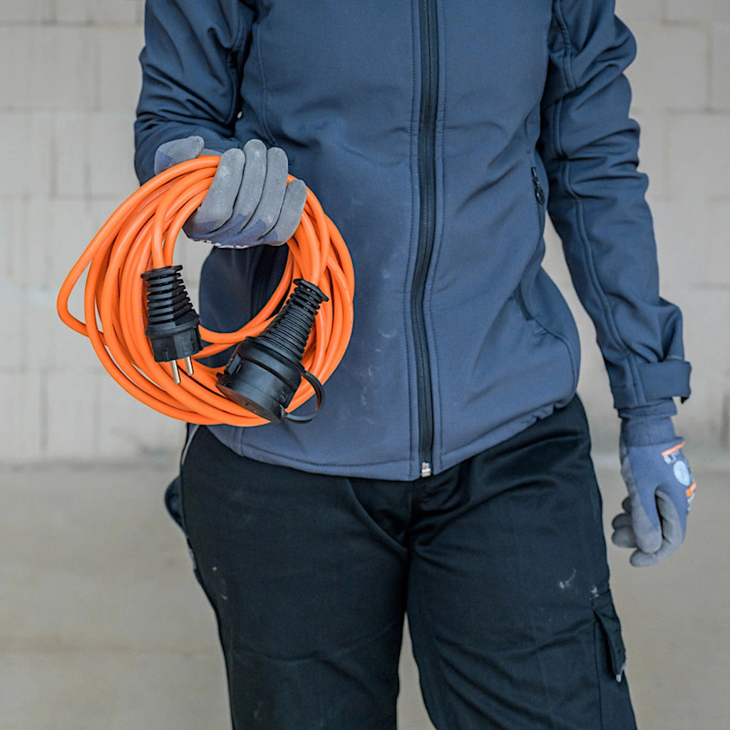 Ein Mann in blauer Arbeitskleidung hat ein aufgerolltes orangenes Verlängerungskabel in seiner rechten Hand.