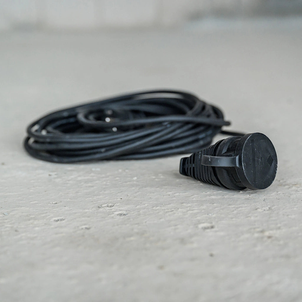 Ein schwarzes Verlängerungskabel liegt zusammengerollt auf dem Betonboden einer Baustelle.