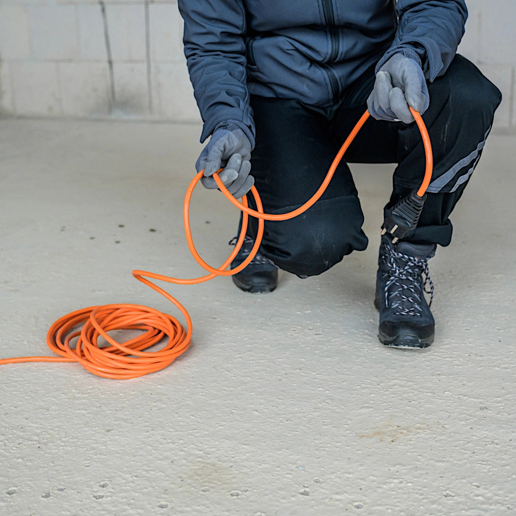 Ein Mann hockt auf einer Baustelle und hält ein orangenes Verlängerungskabel in der Hand.
