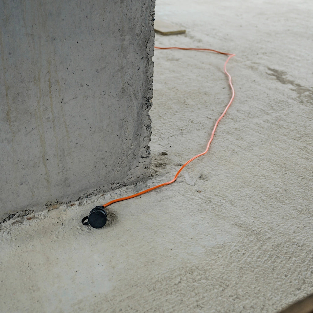 Ein orangenes Brennenstuhl Verlängerungskabel liegt ausgelegt auf dem Betonboten eines Rohbaus.