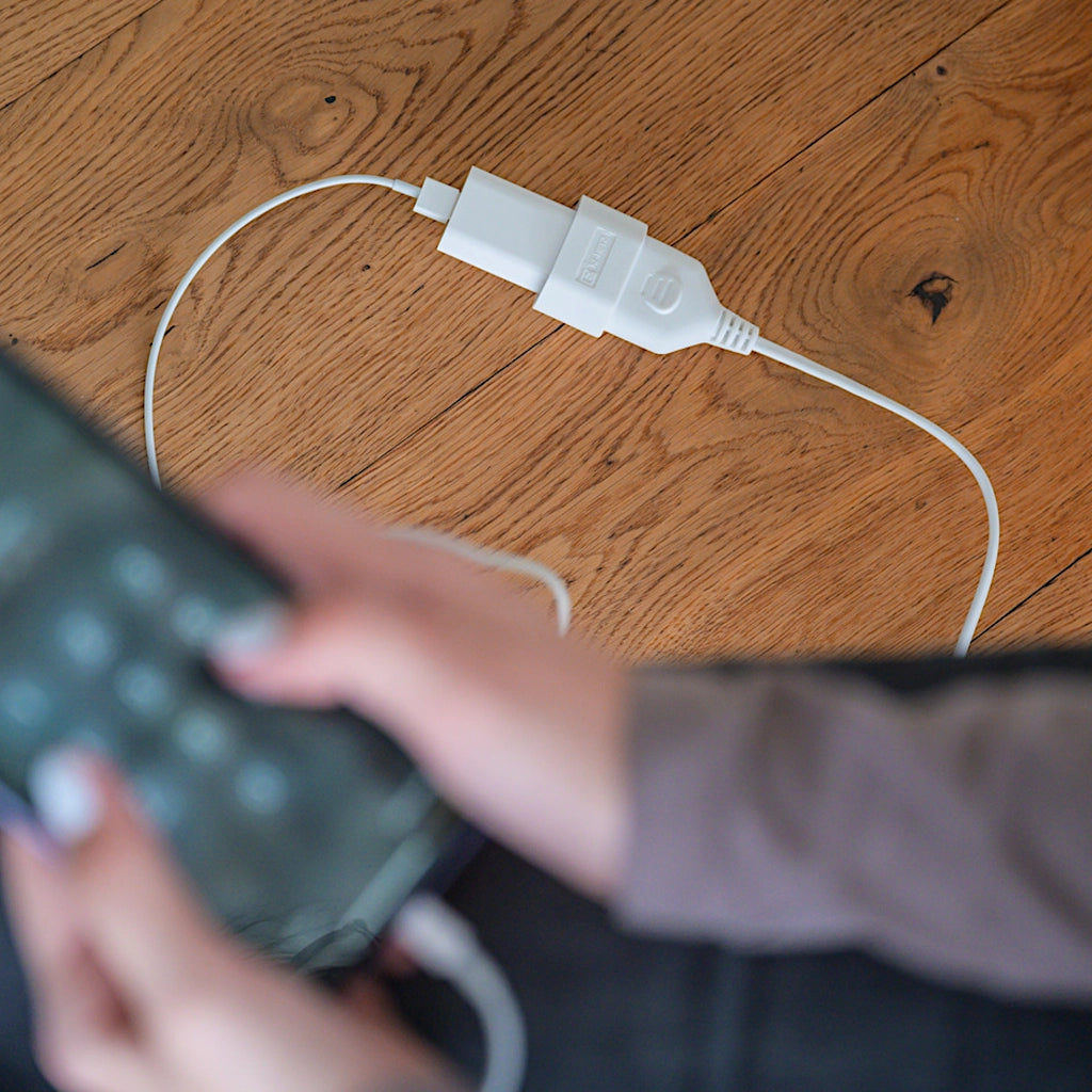 Ein Brennenstuhl Verlängerungskabel in weiß liegt auf dem Holzboden und der Ladestecker von einem Handy ist eingesteckt