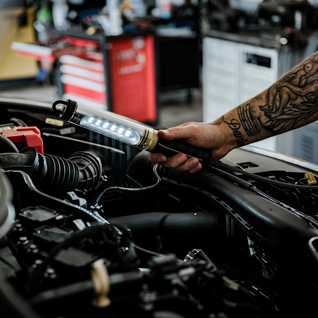 Ein Mitarbeiter in einer Werkstatt leuchte mit der Brennenstuhl Handlampe bei geöffneter Motorhaube in den Motorraum.