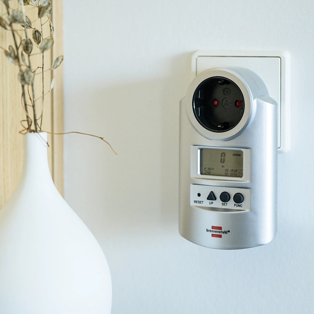 Ein silbernes Brennenstuhl Energiekostenmessgerät steckt an einer weißen Wand in einer Steckdose