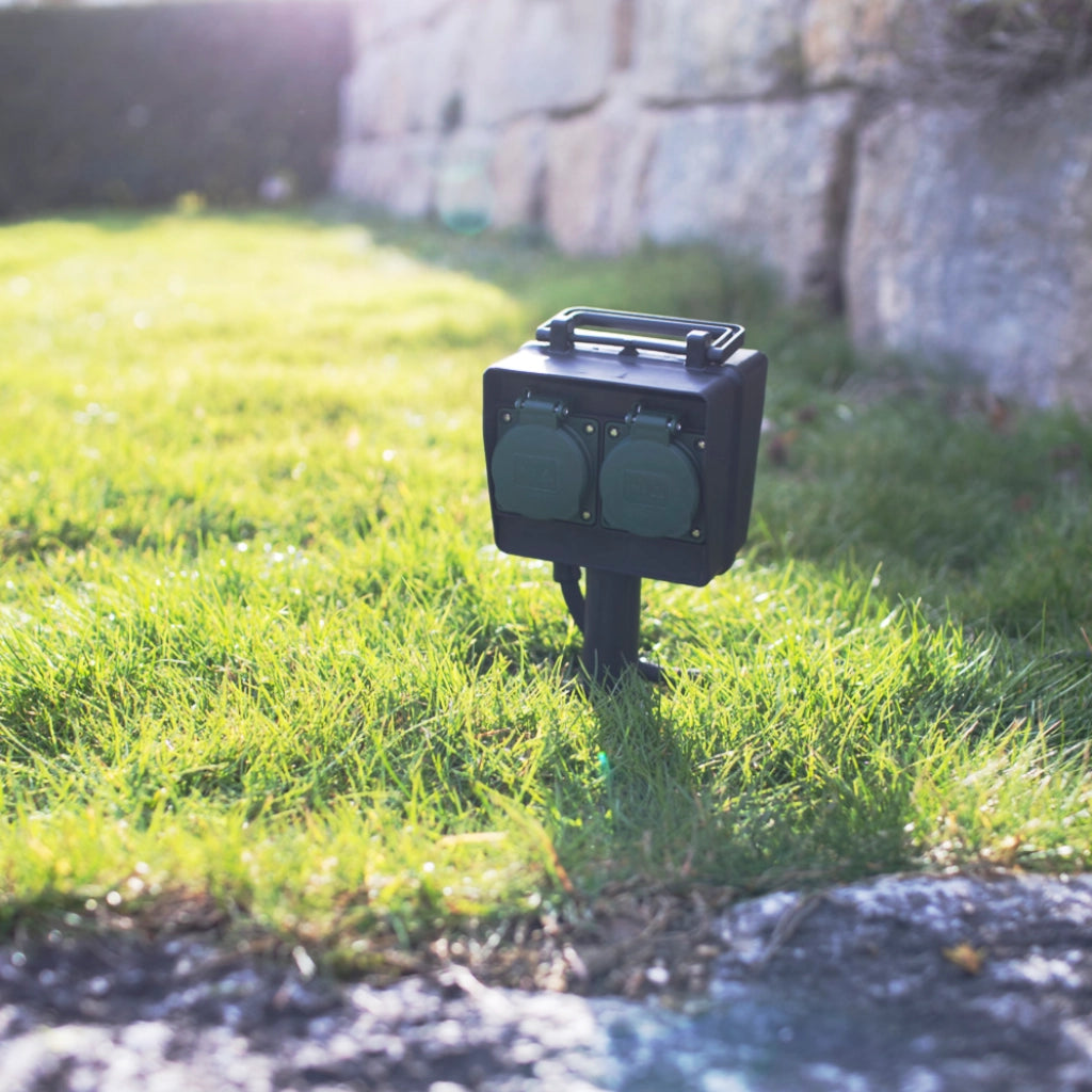 Eine schwarze Brennenstuhl 4-fach Gartensteckdose mit Erdspieß steckt im Rasen - Anicht schräg von vorn