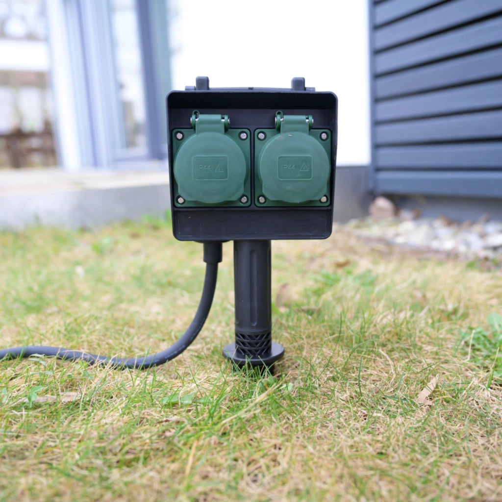 Eine schwarze Brennenstuhl 4-fach Gartensteckdose mit Erdspieß steckt im Rasen - Ansicht von vorn