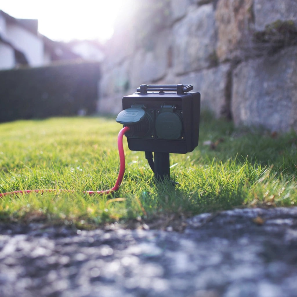 Eine schwarze Brennenstuhl 4-fach Gartensteckdose mit Erdspieß steckt im Rasen mit einem angesteckten Kabel