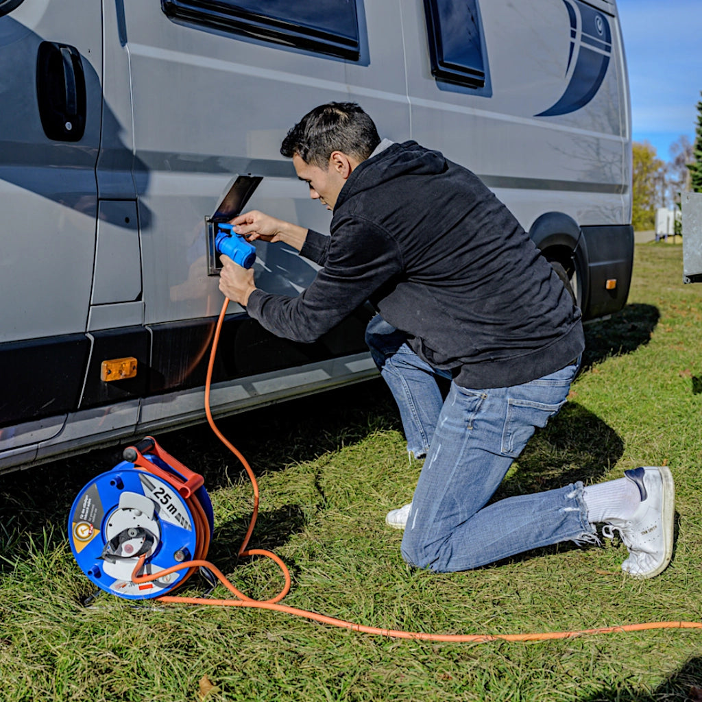 Ein Mann schließt auf einem Campingplatz die Brennstuhl Kabeltrommel ans Wohnmobil an.