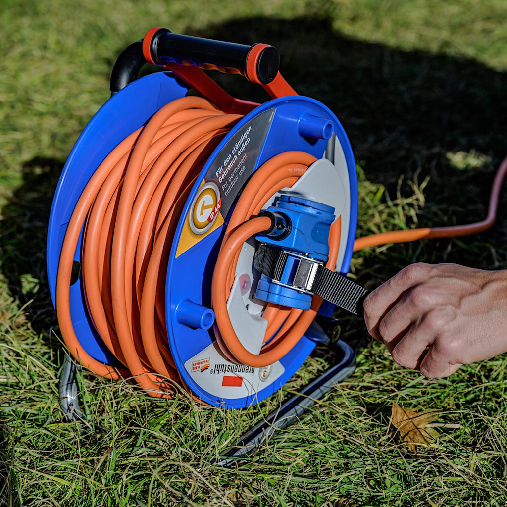 Ein Mann fixiert auf einer Wiese die CEE Kupplung mit einem Gurt an der Brennenstuhl Kabeltrommel