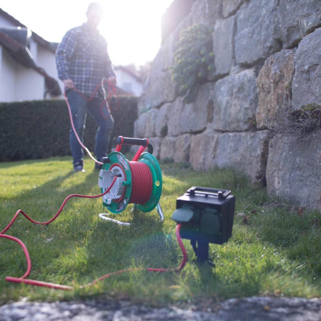 Eine Brennenstuhl Kabeltrommel steht auf einer grünen Wiese und ist an einer Gartensteckdose angeschlossen