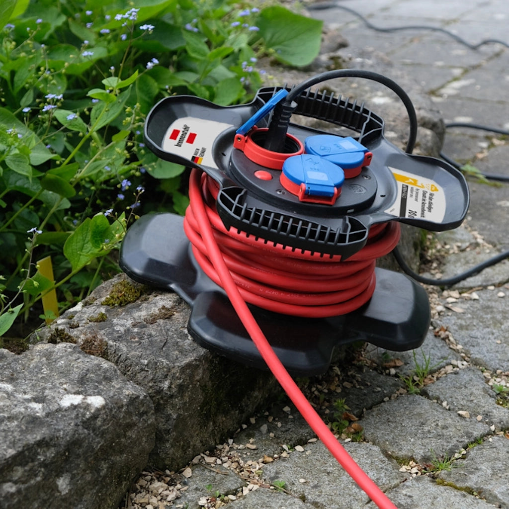 Eine Brennenstuhl X-Gum Kabeltrommel liegt auf einem Weg aus grauen Pflastersteinen