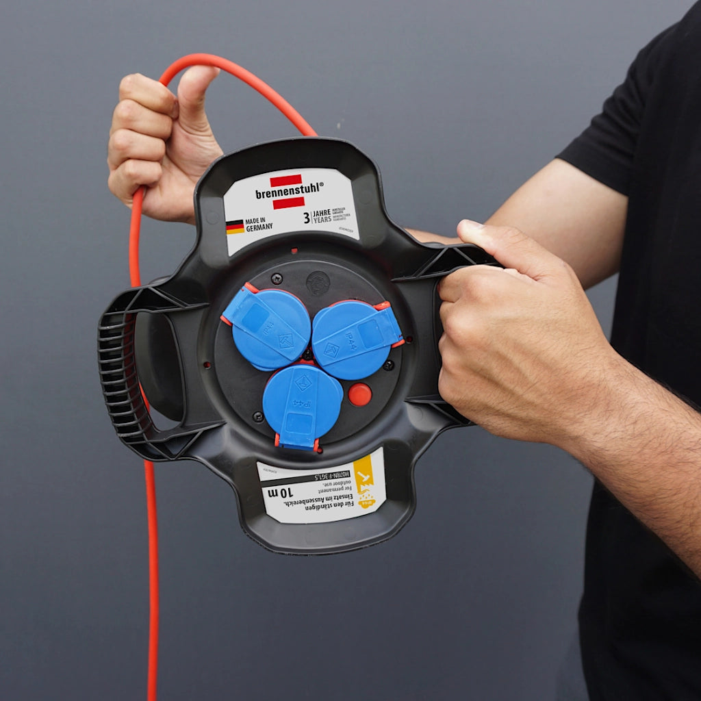 Ein Mann hält eine Brennenstuhl X-Gum Kabeltrommel in der Hand und wickelt das rote Kabel auf