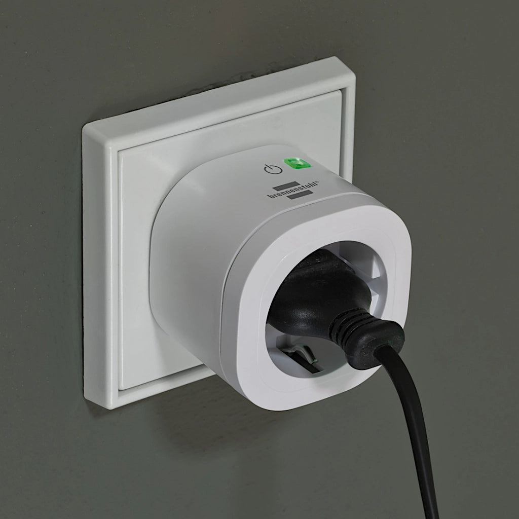 Eine Brennenstuhl WiFi Steckdose eingesteckt ineiner Steckdose an einer grünen Wand mit grün leuchtender LED