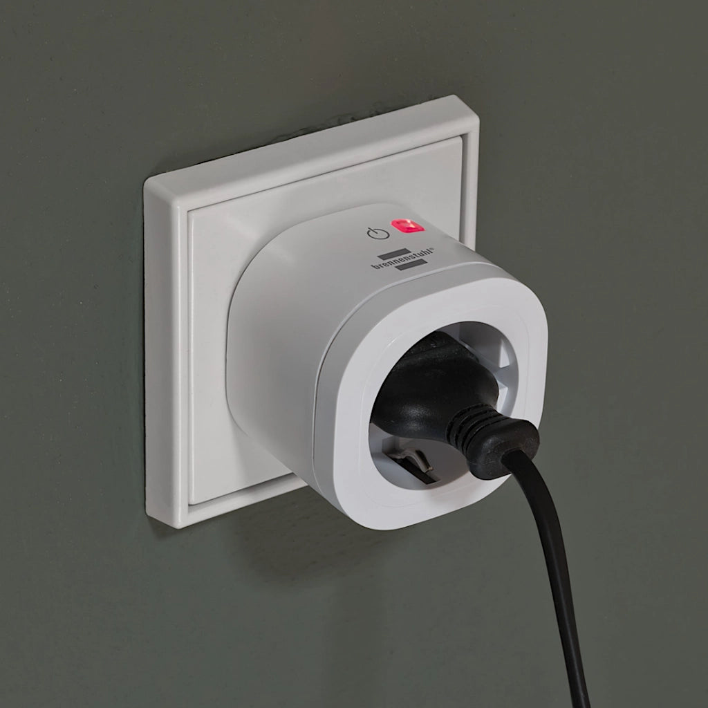 Eine Brennenstuhl WiFi Steckdose eingesteckt ineiner Steckdose an einer grünen Wand mit rot leuchtender LED