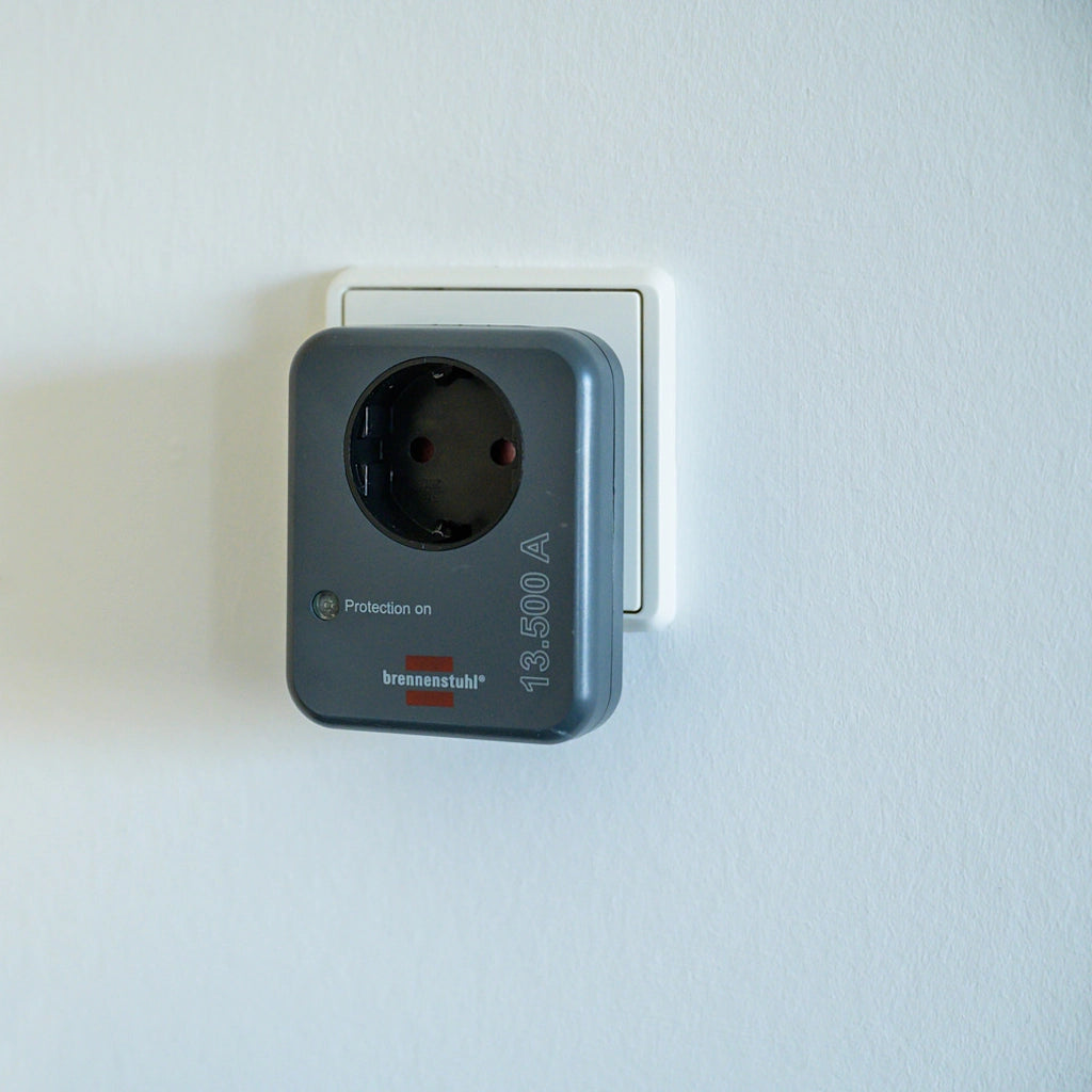 Ein Brennenstuhl Steckdosenadapter mit Überspannungsschutz steckt in einer Wandsteckdose an einer weißen Wand.
