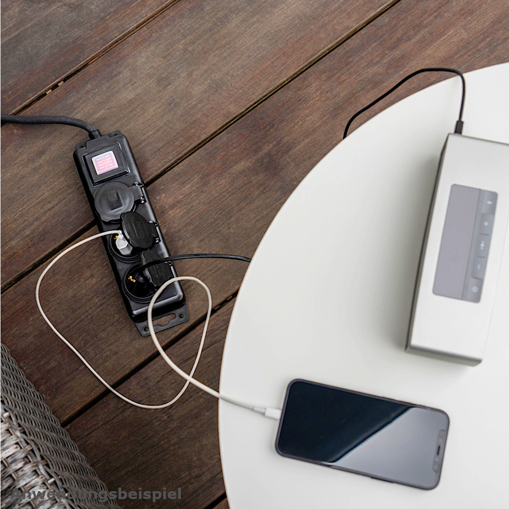 Eine Brennenstuhl Steckdosenleiste in schwarz an der ein Handyladegerät angeschlossen ist, liegt auf einem braunen Holzfußboden