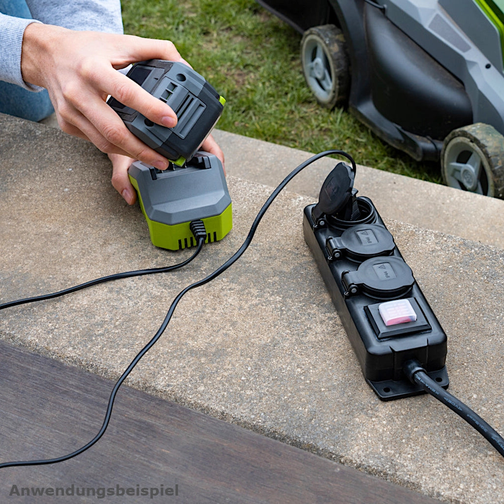 Eine Brennenstuhl Steckdosenleiste in schwarz an der ein Akku-Lädegerät eingesteckt ist, liegt auf einer Betonstufe im Garten