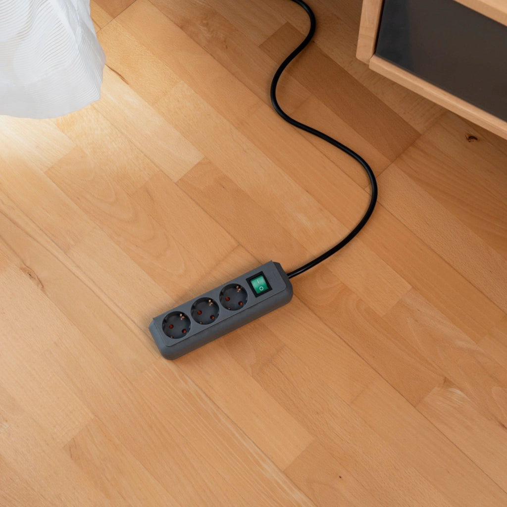 Eine silbergraue Brennenstuhl Eco-Line Steckdosenleiste 3-fach mit Schalter liegt auf einem Holzfußboden