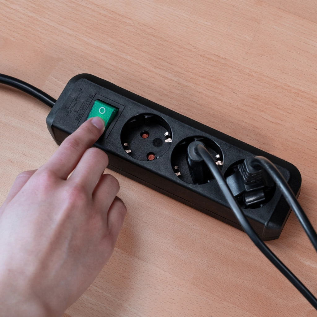 Ein Mann betätigt den Ein- und Ausschalter einer schwarzen Brennenstuhl 3-fach Steckdosenleiste