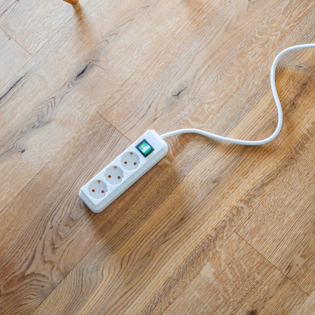 Eine weiße Brennenstuhl Eco-Line Steckdosenleiste 3-fach mit Schalter liegt auf einem Holzfußboden
