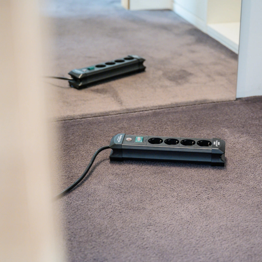 Eine Brennenstuhl Steckdosenleiste 4-fach mit Schalter liegt auf einem braunem Teppich vor einem Spiegel