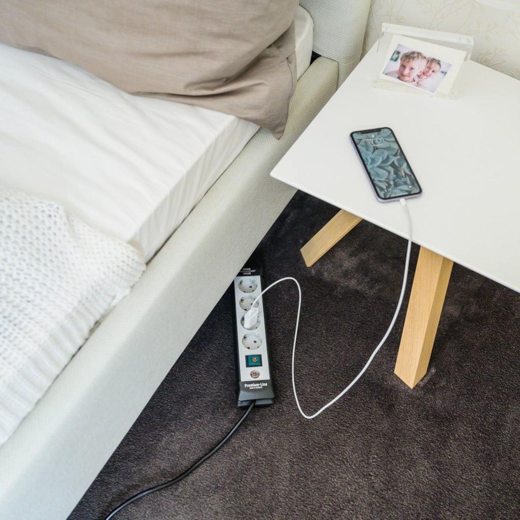 Eine Brennenstuhl Steckdosenleiste 4-fach mit Schalter liegt auf einem Teppich vor einem Bett