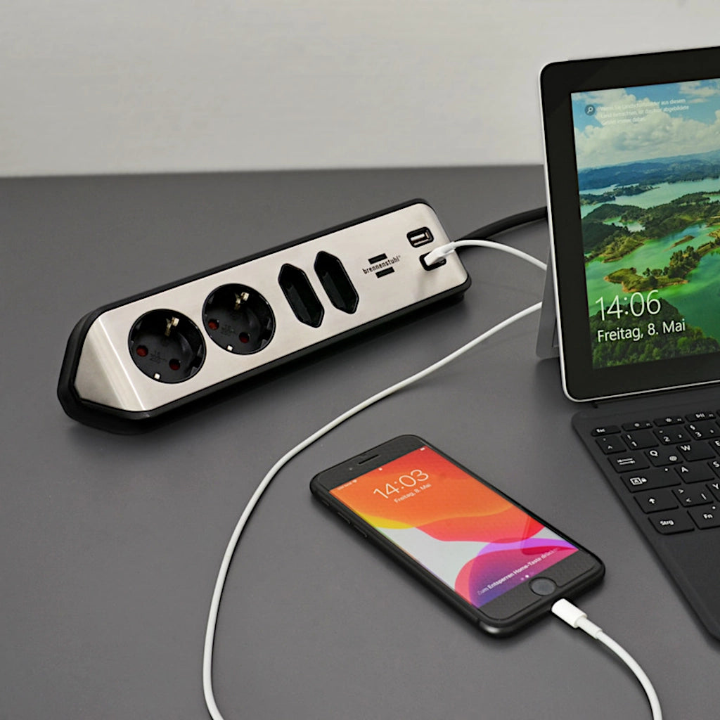 Eine Brennenstuhl Eck-Steckdosenleiste liegt zusammen mit einem Handy und einem Laptop auf einem grauen Tisch