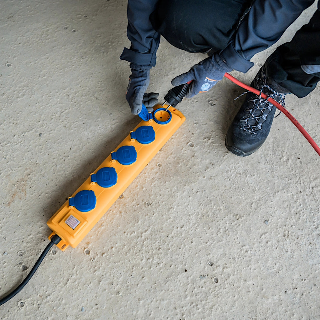 Eine gelbe Steckdosenleiste mit blauen Deckeln liegt auf einem Rohbetonboden 