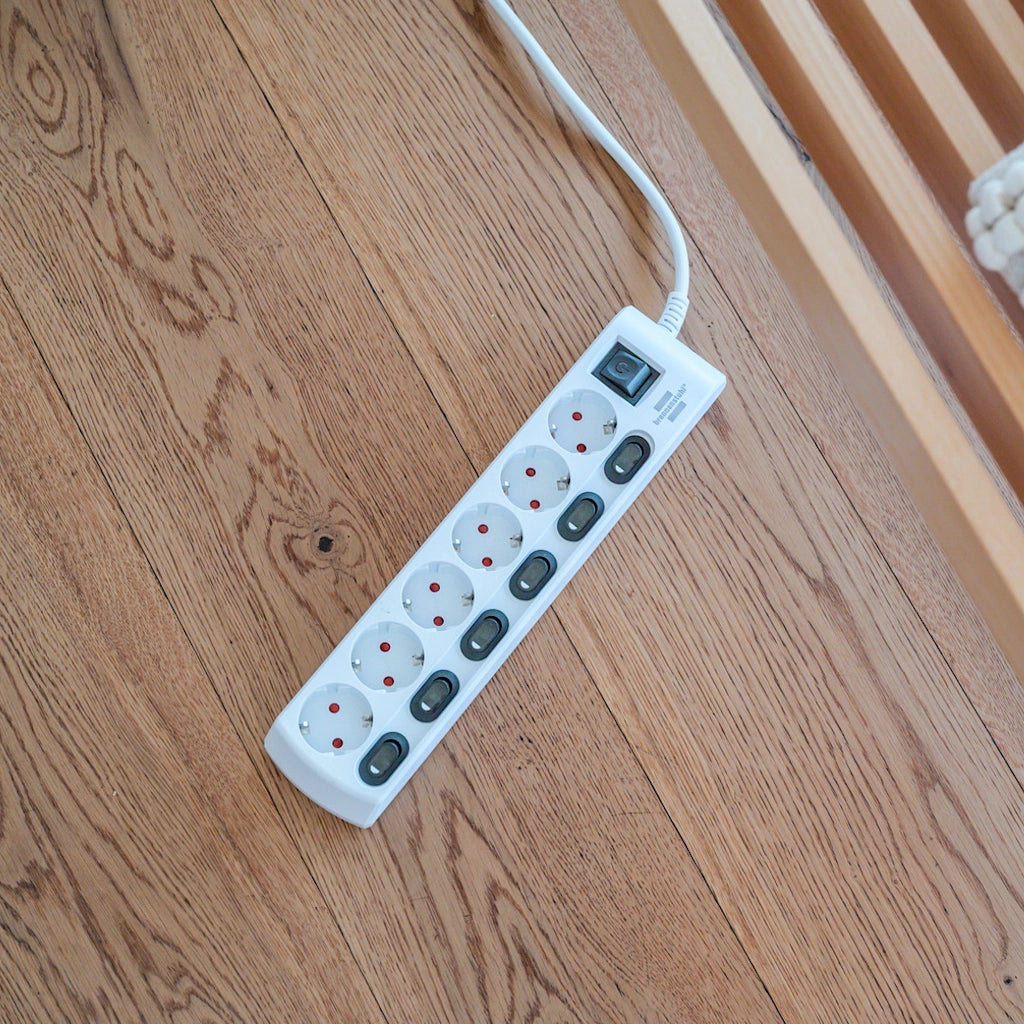 Eine weiße Brennenstuhl 6-fach Steckdosenleiste liegt auf einem Holzfußboden