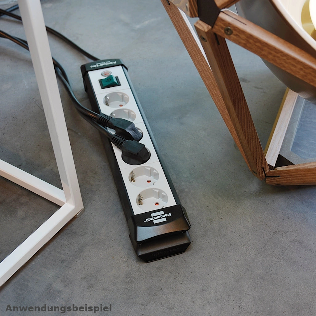 Eine Brennenstuhl Steckdosenleiste 6-fach mit Schalter liegt auf einem blauen Teppich zwischen 2 Stühlen