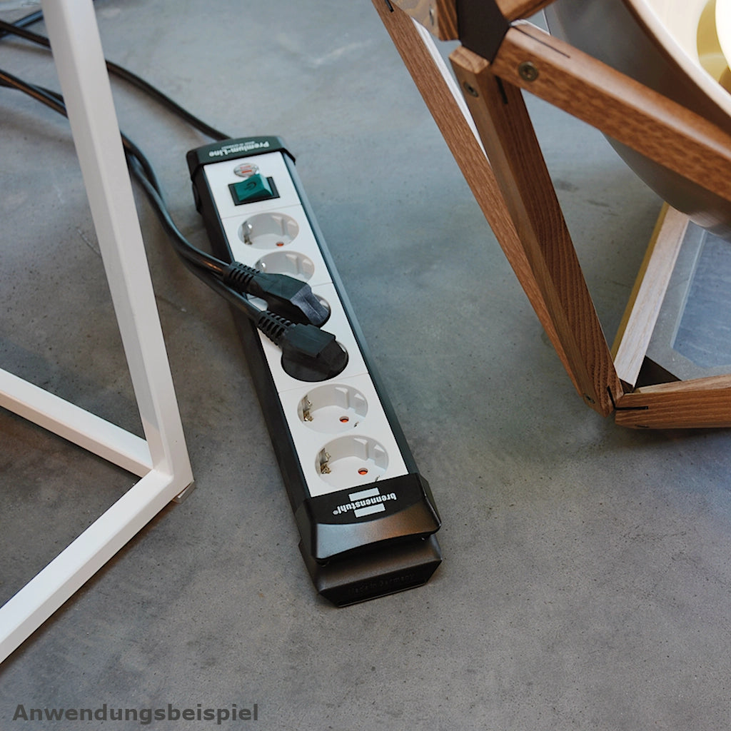 Eine Brennenstuhl Steckdosenleiste 6-fach mit Schalter liegt auf einem blauen Teppich zwischen 2 Stühlen