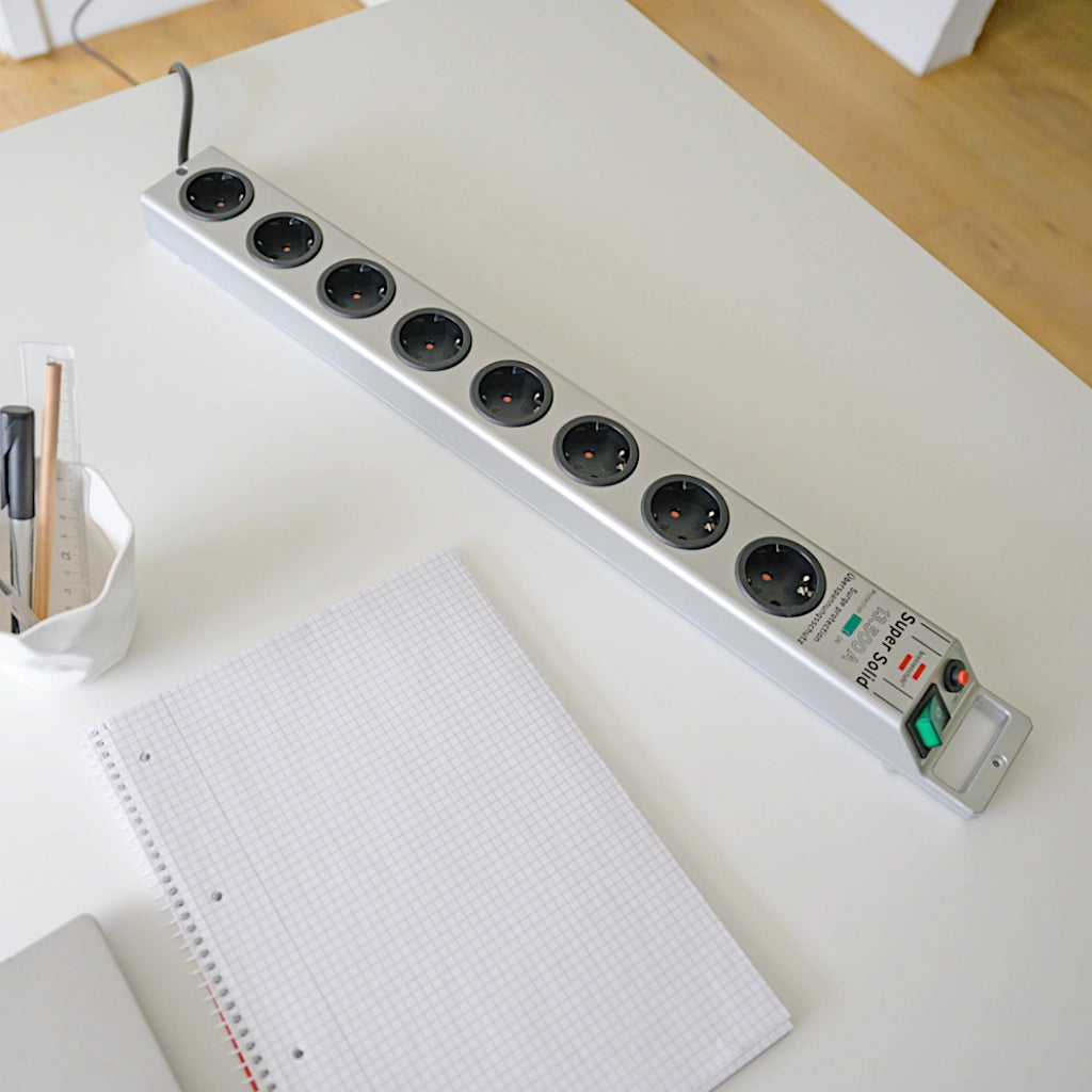 Eine silberne Brennenstuhl Steckdosenleiste mit Überspannungsschutz liegt auf einem Schreibtisch