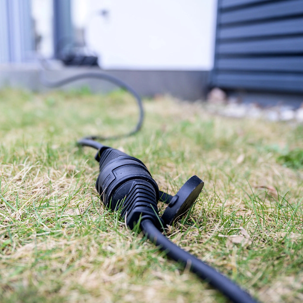Ein schwarzes Verlängerungkabel für außen liegt auf einer grünen Wiese.