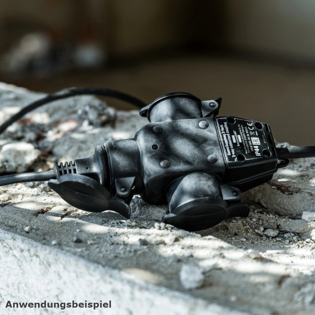 Eine schwarze Brennenstuhl 3-fach Kupplung mit einem eingesteckten Stecker liegt auf ein Rohbetonwand