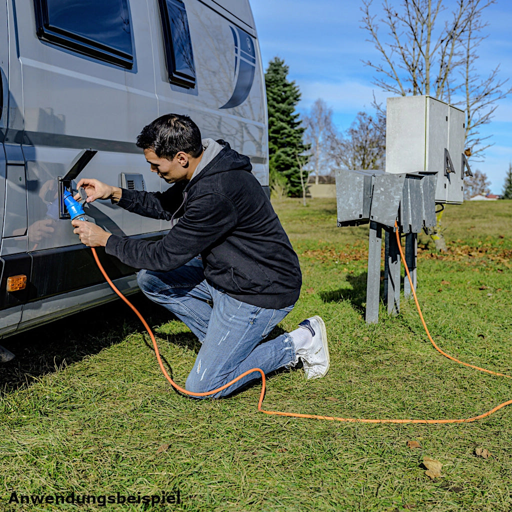 Ein Mann kniet vor einem weißen Wohnmobil und schließt eine Brennenstuhl Camping Verlängerungskabel in orange an
