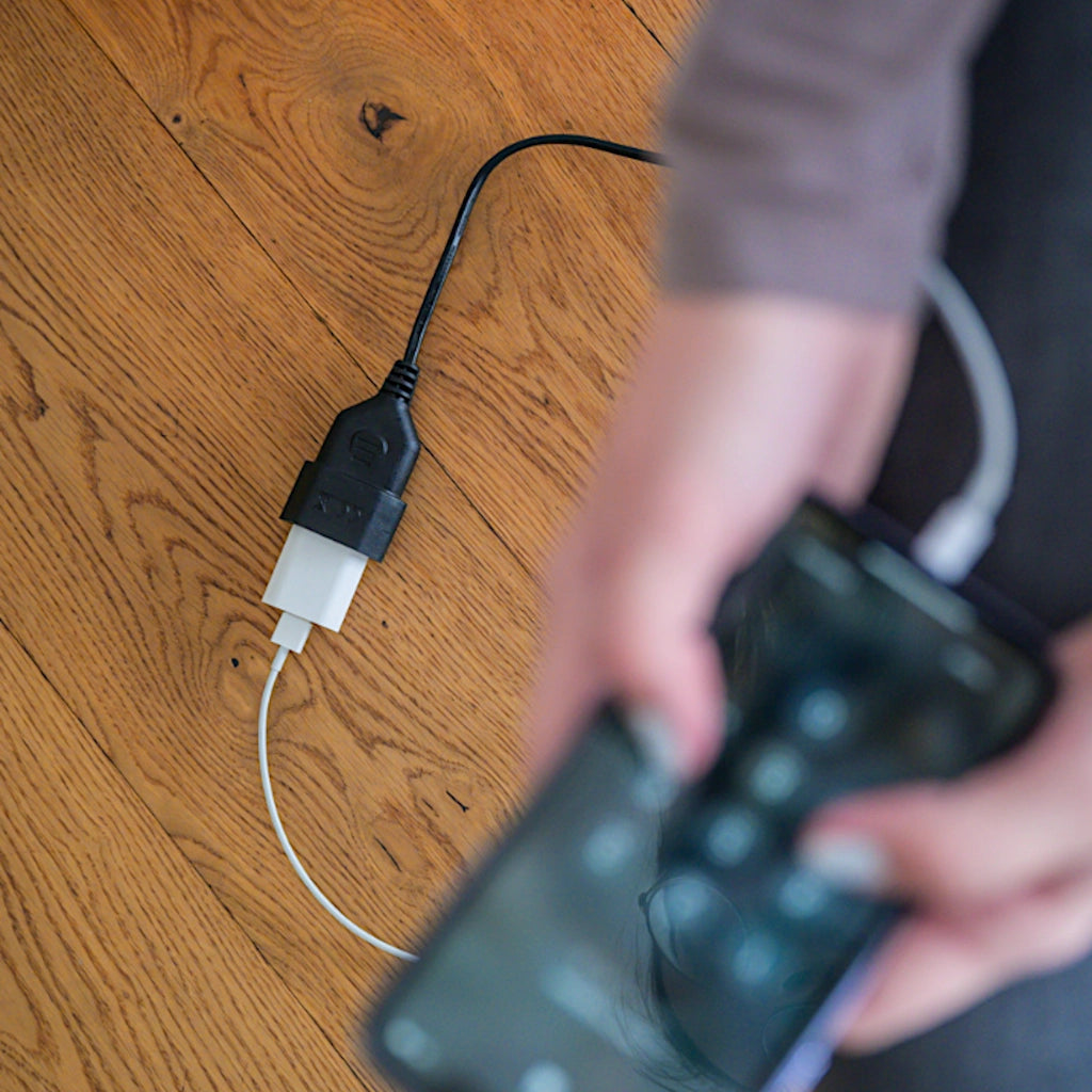Ein Brennenstuhl Verlängerungskabel in schwarz liegt auf dem Holzboden und der Ladestecker von einem Handy ist eingesteckt