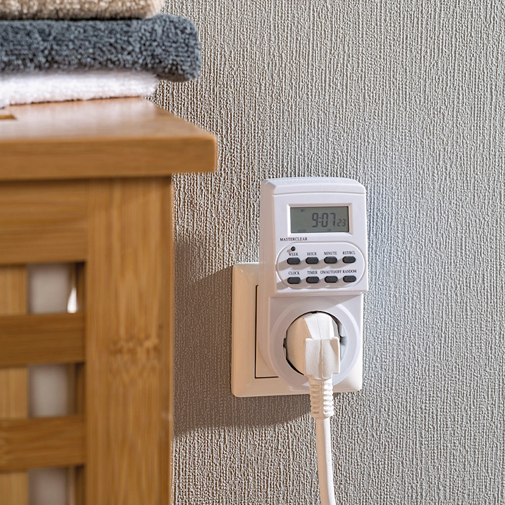 Eine weiße digitale Brennenstuhl Zeitschaltuhr steckt an einer weißen Wand in einer Steckdose mit eingestecktem Stecker
