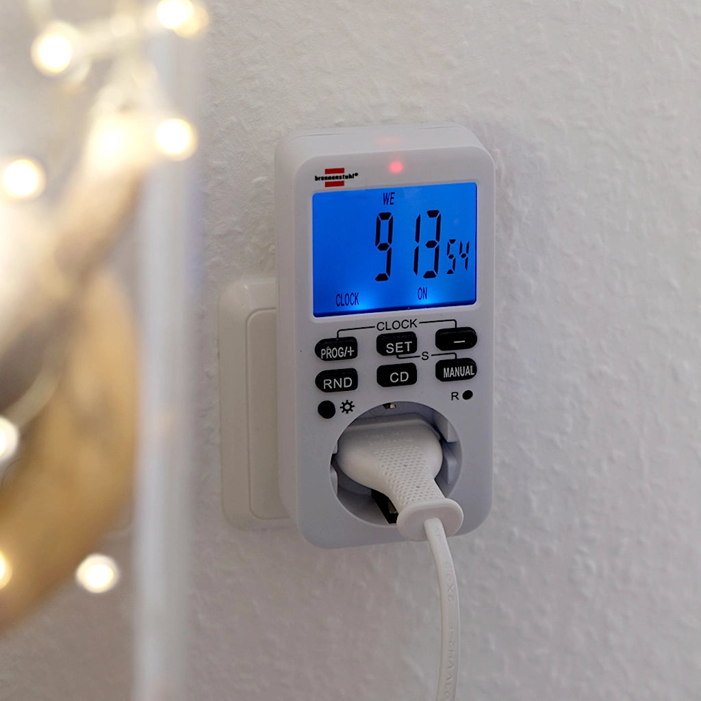Eine digitale Brennenstuhl Zeitschaltuhr mit beleuchteten Display in weiß steckt an einer weißen Wand in einer Steckdose